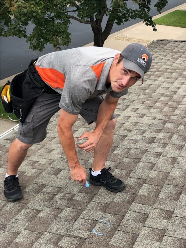 Worker inspecting and marking roof shingles with chalk.