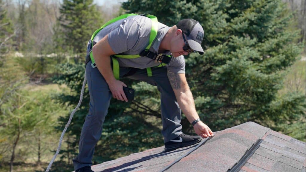 Worker inspecting roof with safety harness.