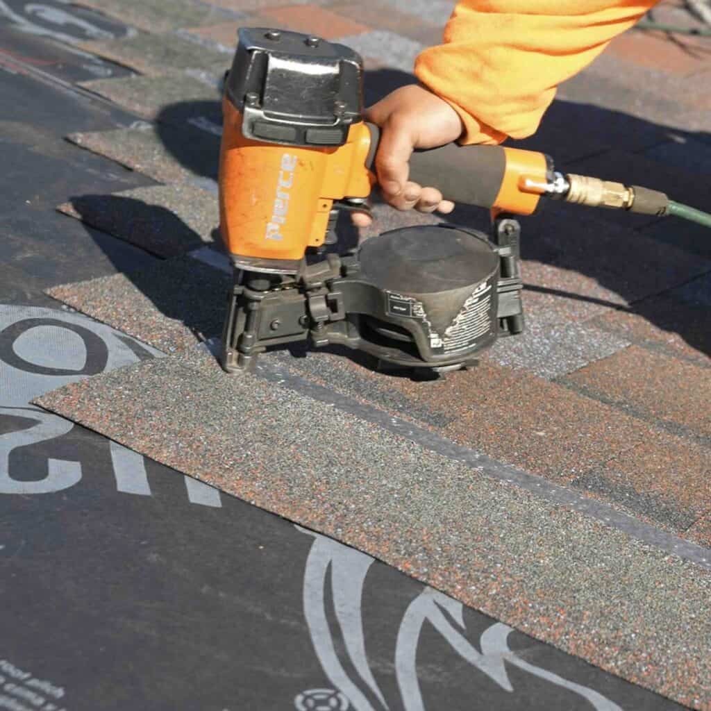 Person using nail gun on roof shingles.