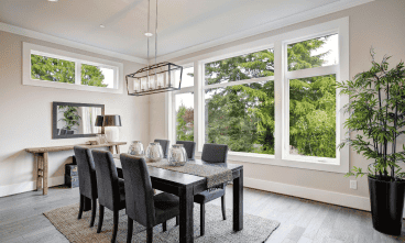 Modern dining room with large windows and greenery.