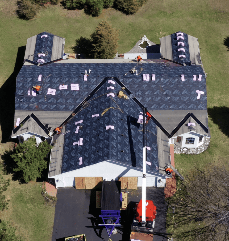 Workers installing new roof shingles on large house.