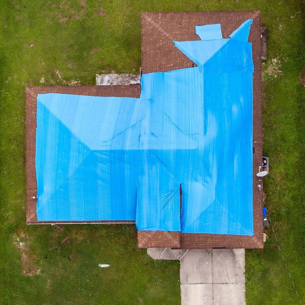 Aerial view of house roof covered with blue tarp