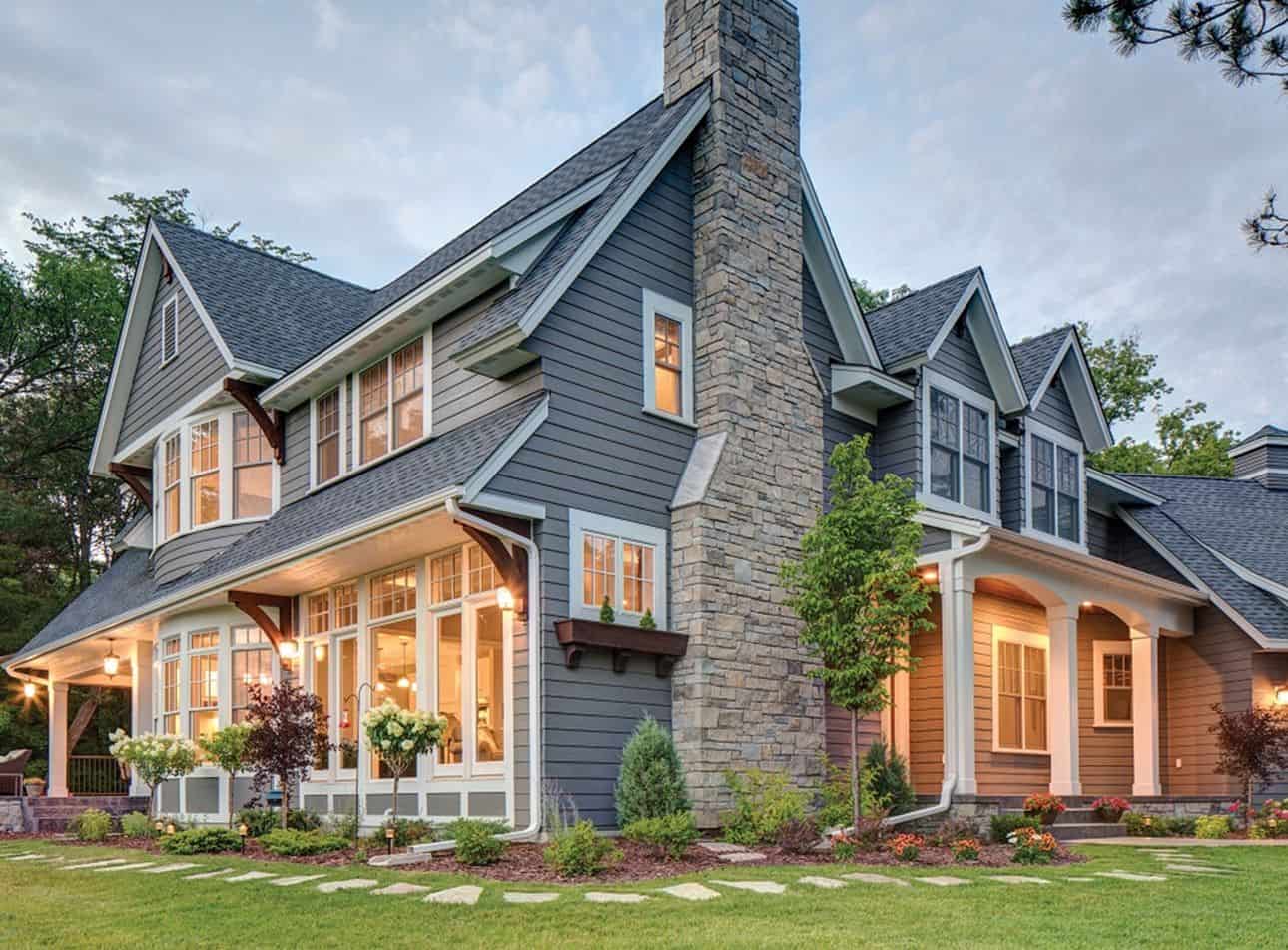 Gray Craftsman home with stone chimney at dusk