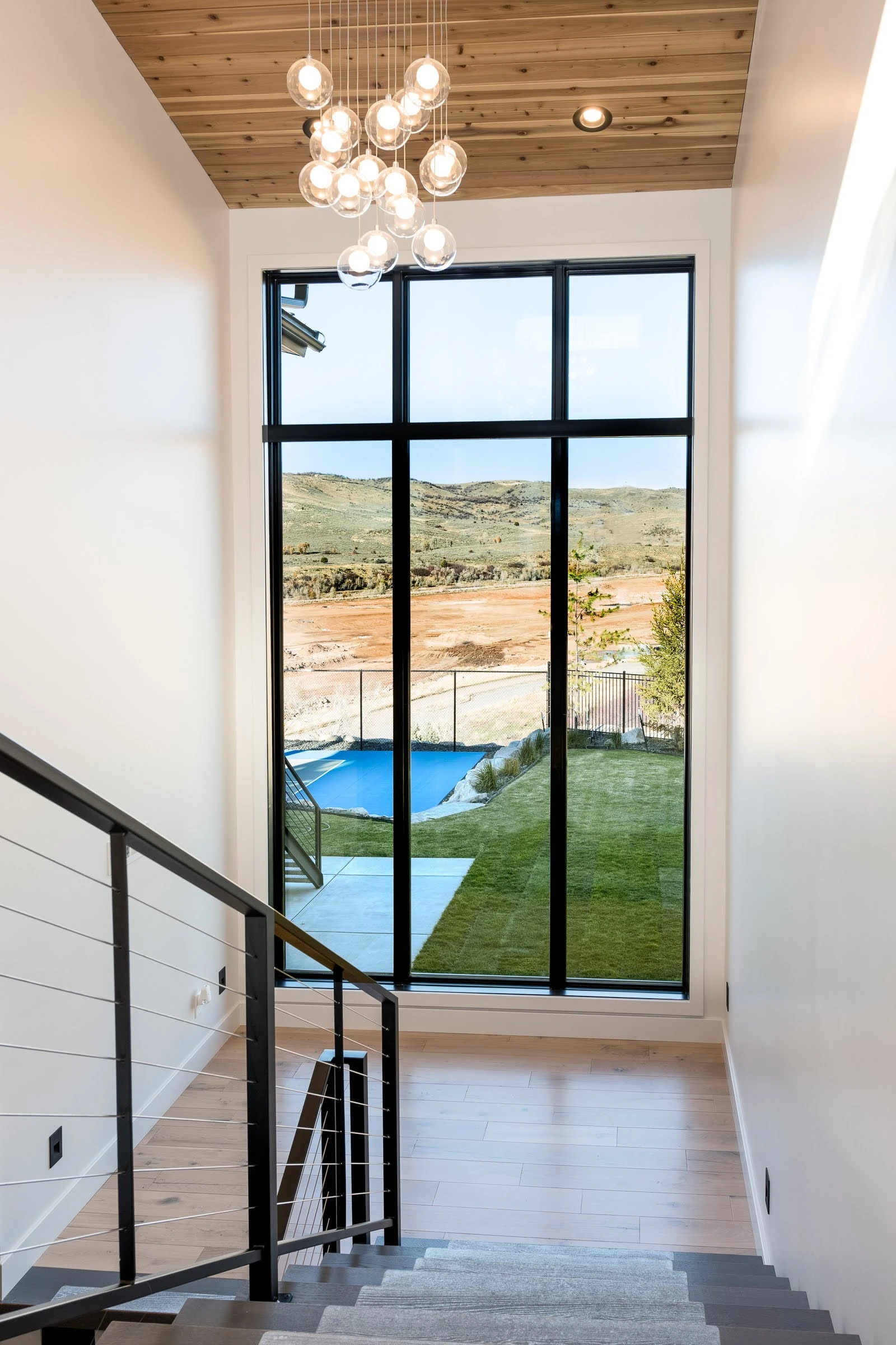 Modern stairwell with chandelier and tall window overlooking hills
