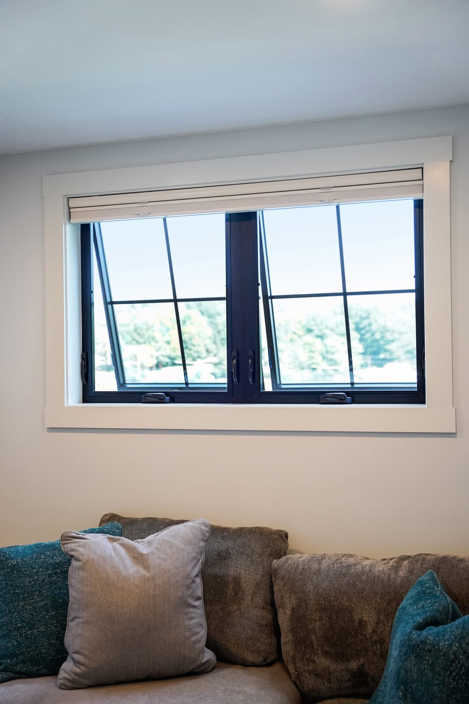 Open black-framed window above gray sofa with pillows